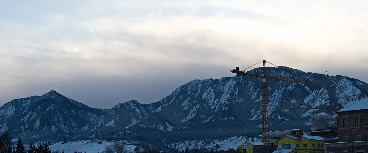 Photo: the Flatirons above Boulder in winter with a tower crane on a campus building site