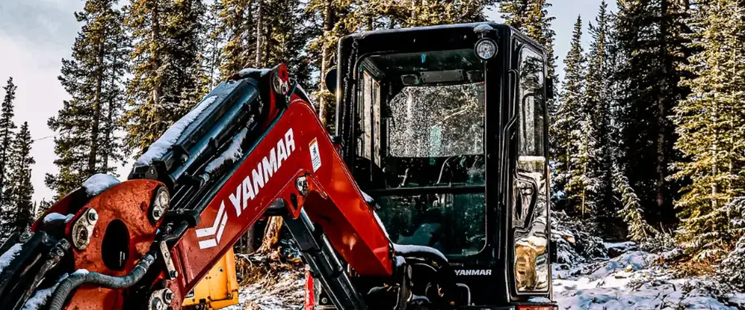 Photo: a mini excavator working in fresh snow under spruce on a high-country lot
