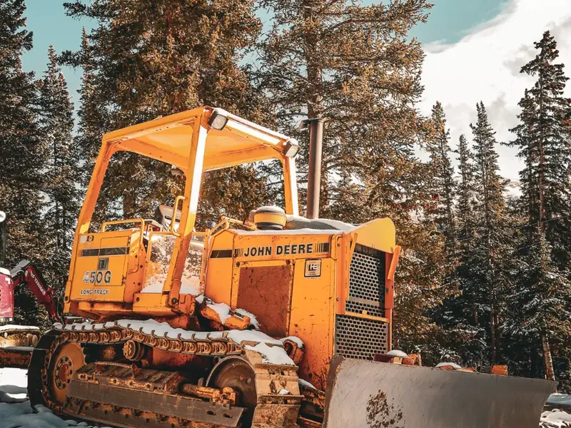 Photo: a dozer with a blade parked in snow under pines