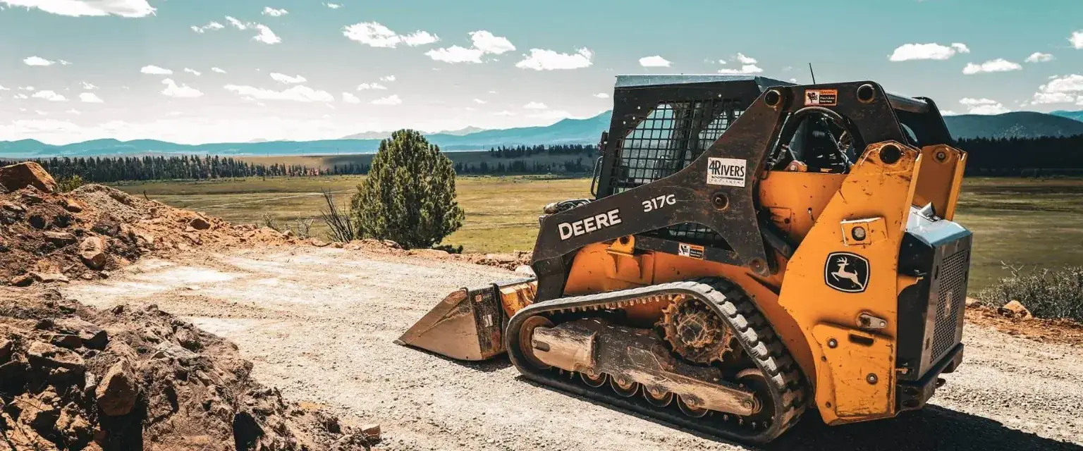 Photo: a compact track loader on a graded pad in the South Park valley with mountains behind