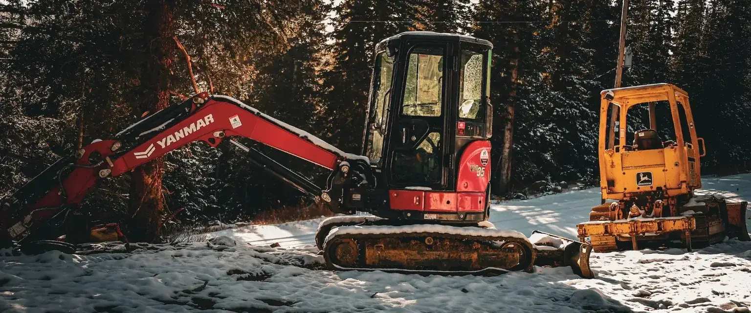 Photo: a mini excavator and a track loader parked in fresh snow at a mountain job site