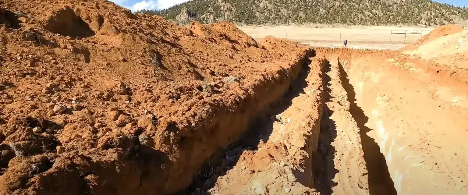 Photo: an open utility trench cut through red mountain soil on a Park County job